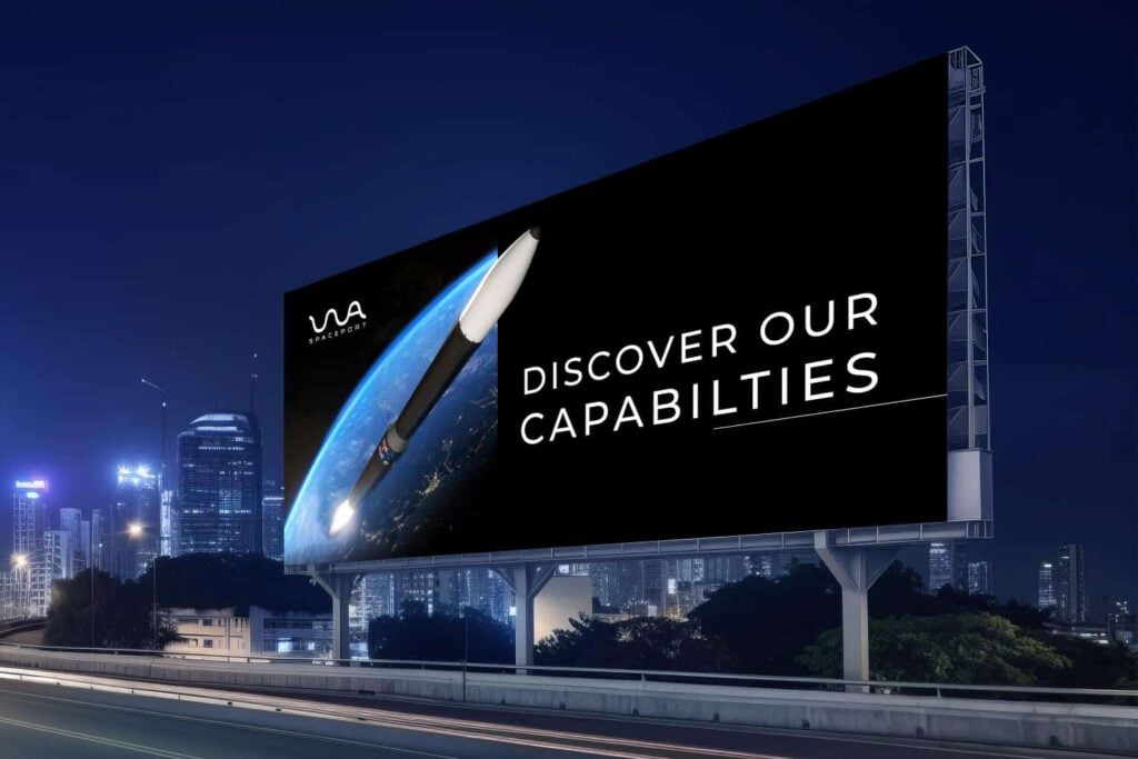 A large hoarding in a city at night displays a rocket launching with the text DISCOVER OUR CAPABILITIES, highlighting WA Spaceport, and a logo reading VIA AEROSPACE in the top left corner.